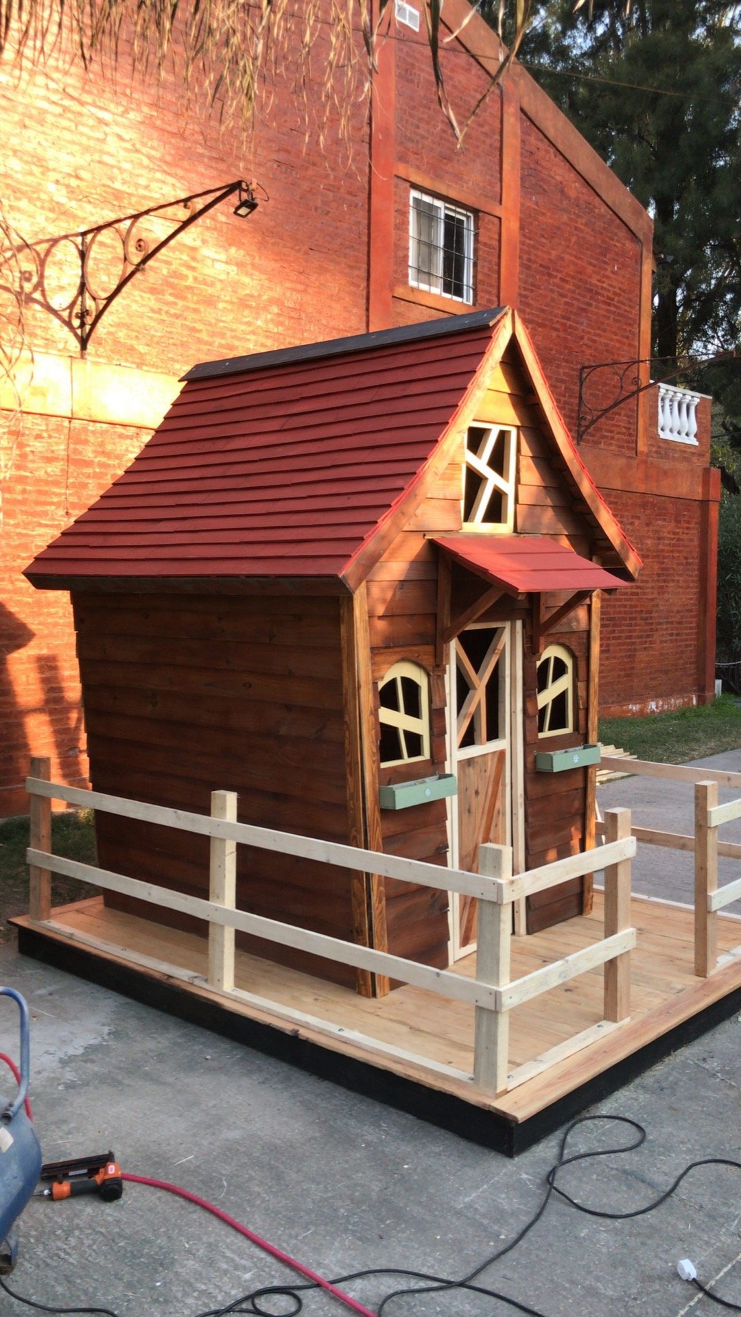 Casita con techo rojo, baranda y deck rodeada de cerca de madera