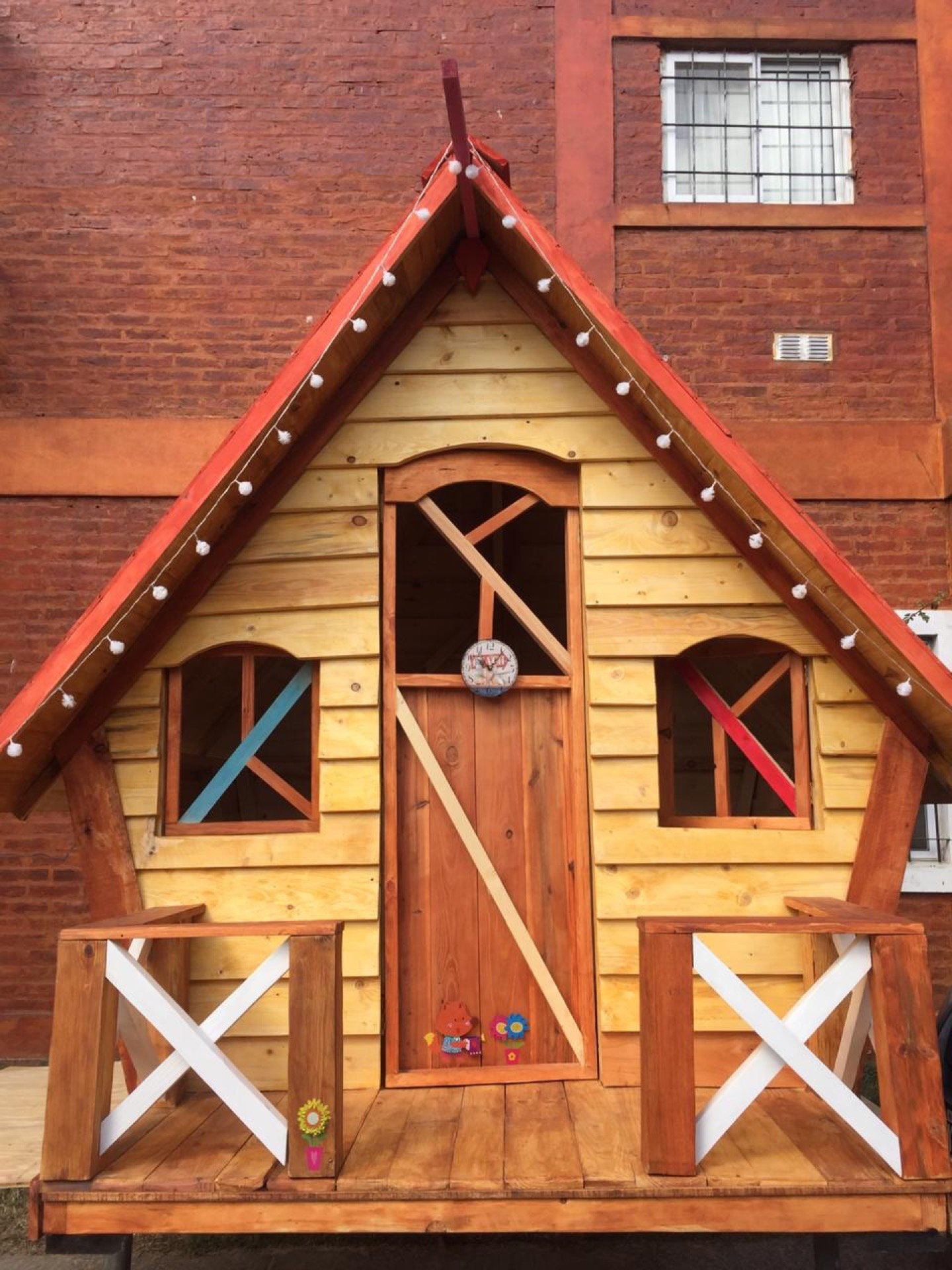 Casita de madera con techo a dos aguas y guirnalda de luces cálidas al atardecer